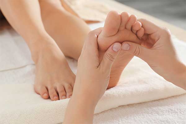 Close reflexology work on a client's foot on a soft, draped massage table